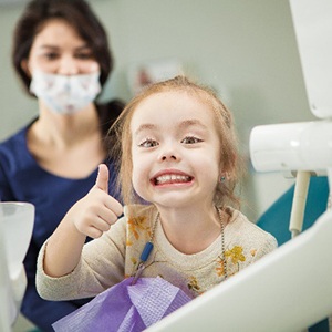 Child giving a big thumbs up while sitting in dental chair