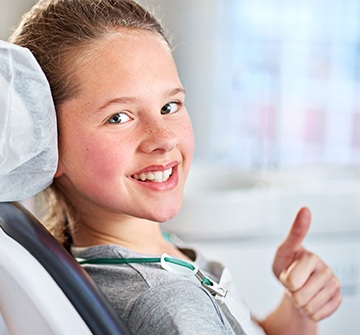 Smiling girl giving thumbs up after dental checkups and teeth cleaning