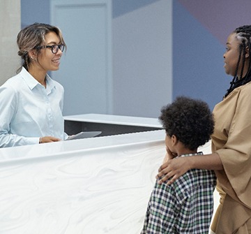 Mom and son talking to smiling dental receptionist about cost