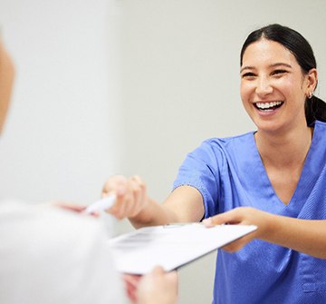 Dental assistant smiling while handing patient form