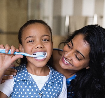Mom smiling at her daughter while brushing her teeth