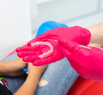 A dental professional holding an Invisalign aligner while explaining to a teen how it works