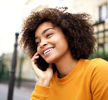 A young female wearing an orange blouse and talking on her cell while showing off her newly aligned smile