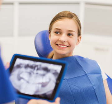 Teen girl smiling at dentist holding X-ray