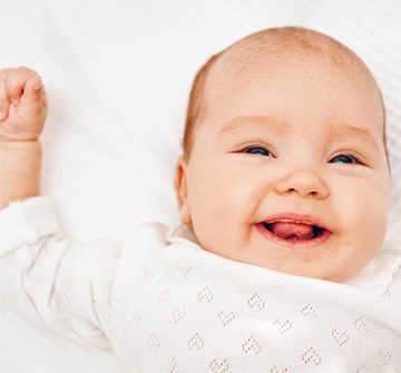 A smiling, happy baby lying on its back and showing its tongue after laser frenectomy