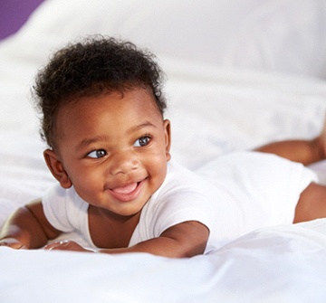 A small baby lying on its stomach on a bed and smiling after laser frenectomy