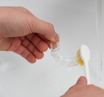 Patient cleaning clear aligner in sink