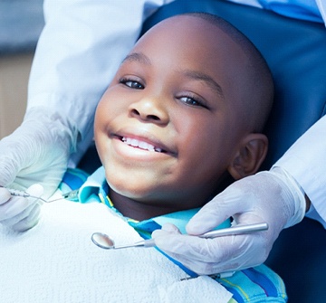 child sitting in a treatment chair while their dentist examines their teeth after emergency dentistry treatment