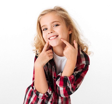 A young girl pointing at her smile after phase one orthodontics