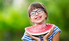 Smiling girl with traditional braces orthodontics holding a watermelon slice