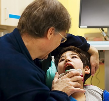 Dentist examining young boy's smile during special needs dentistry visit