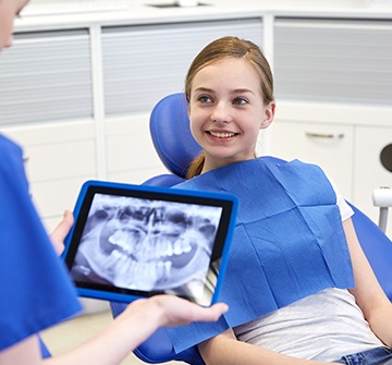 Teen girl in dental chair with x-rays on tablet computer