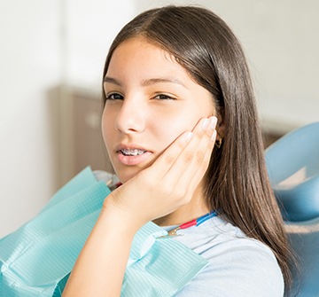 Young woman in dental chair holding cheek in pain during emergency dentistry visit