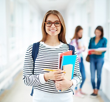 Smiling teen girl holding books at school after dental crown treatment