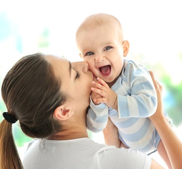 A woman holding up her teething baby while it smiles