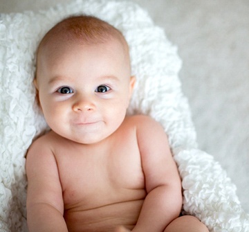 A teething baby laying on a blanket smiling