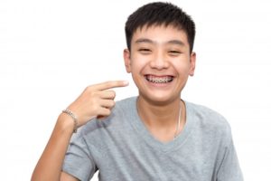 boy in gray t-shirt smiling and pointing to his braces in Nashua 