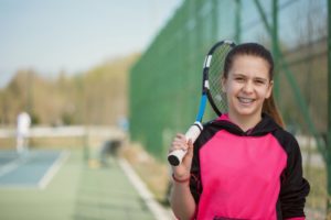 girl with tennis racket playing sports with braces