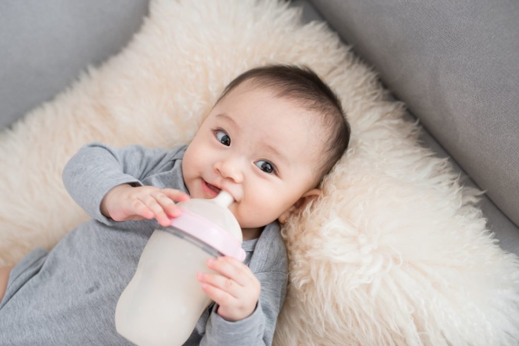 Closeup of baby drinking bottle while lying down on bed
