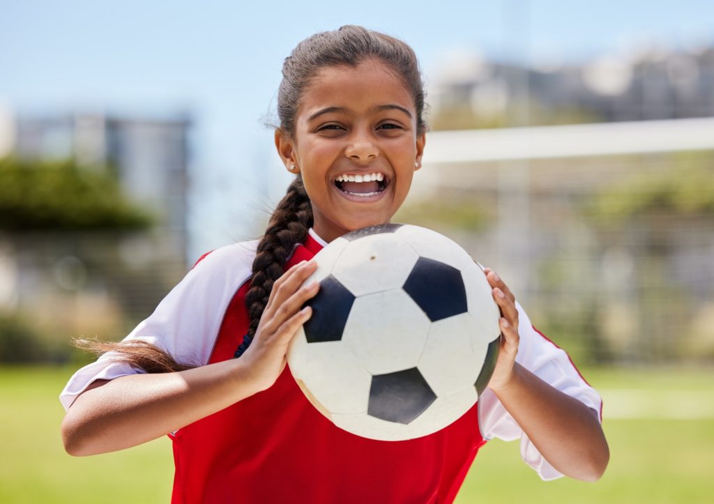 Child smiling while holding soccer ball in red and white jersey