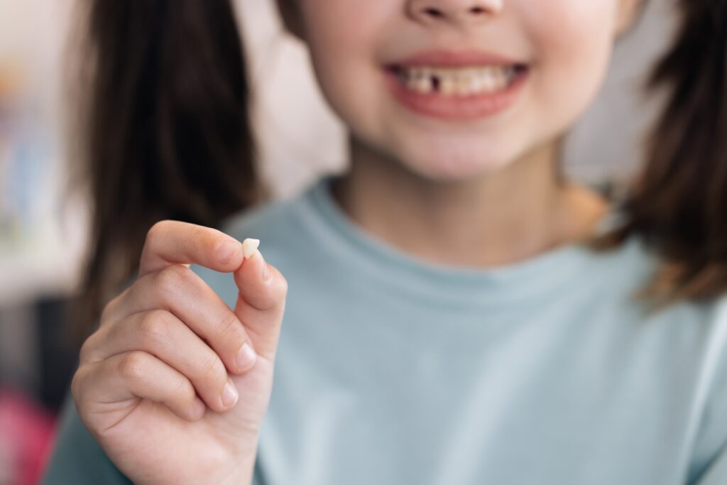 Child holding baby tooth and smiling