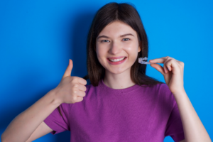 a teen smiling and holding their Invisalign aligner